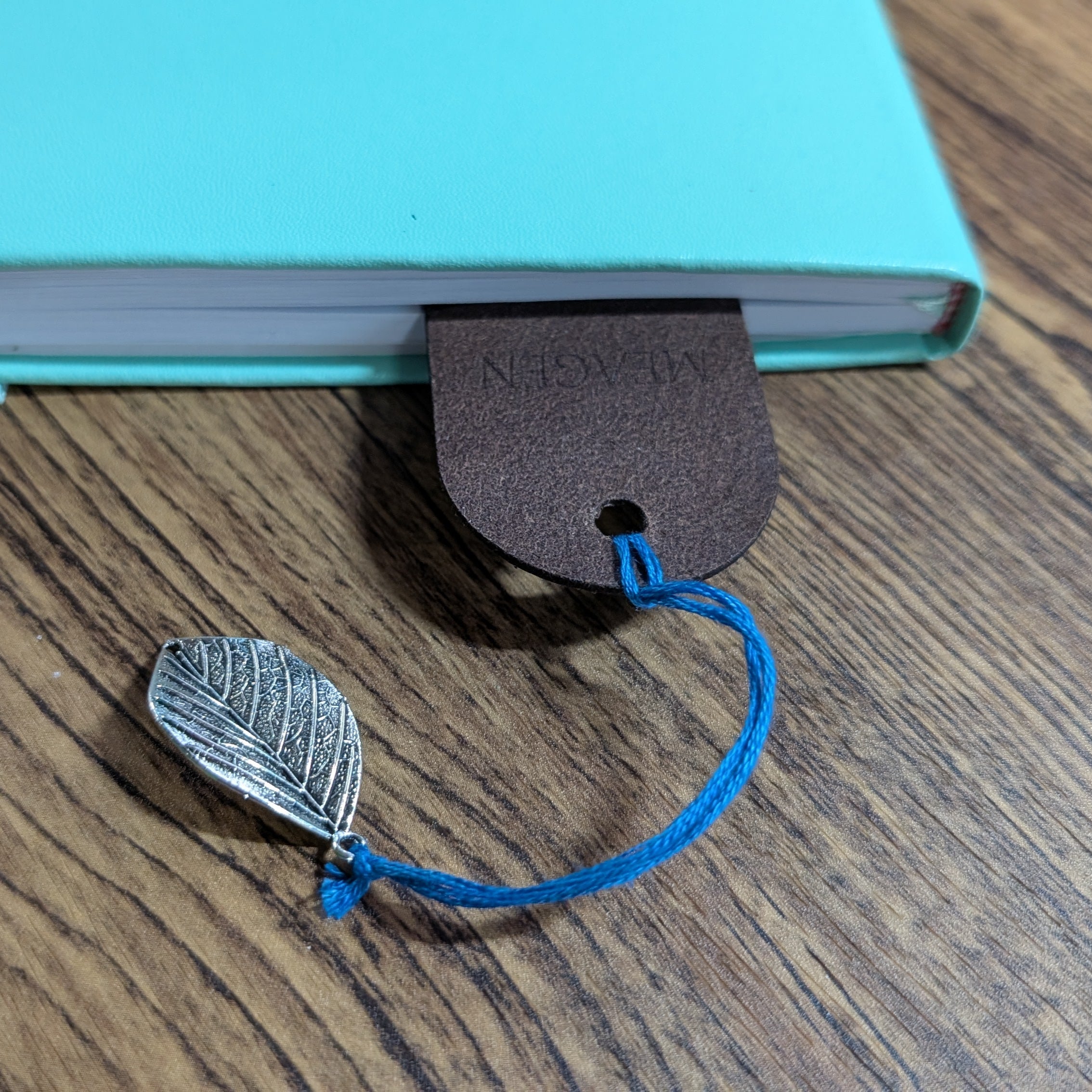 Close-up of a leather bookmark with a blue cord and a silver leaf charm