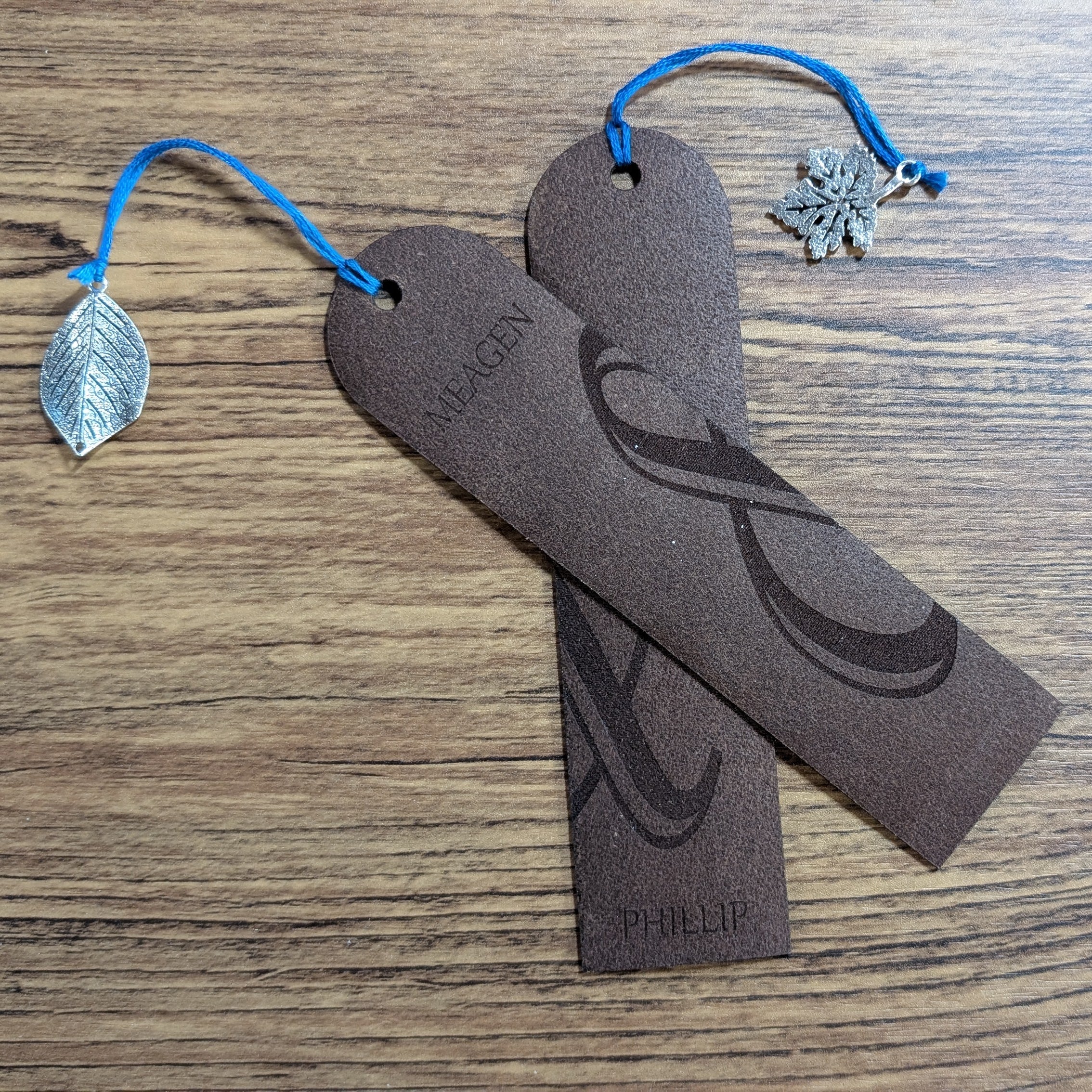 Overlapping pair of personalized leather bookmarks with blue cords and silver charms